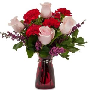 A romantic mixture of pink roses, red carnations and heather in a red vase